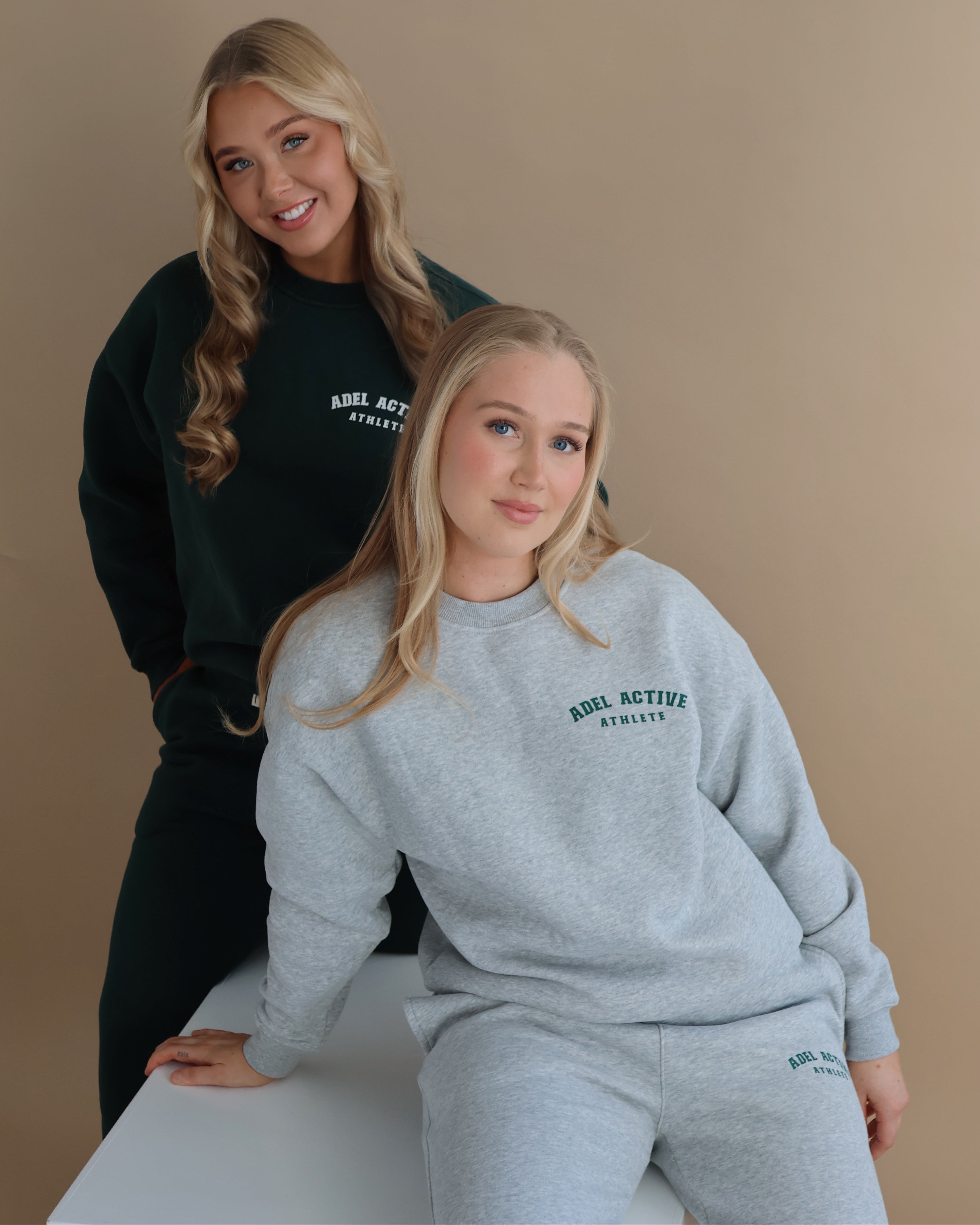 Two individuals wearing 'Adel Active' branded sweatshirts and pants on a beige background